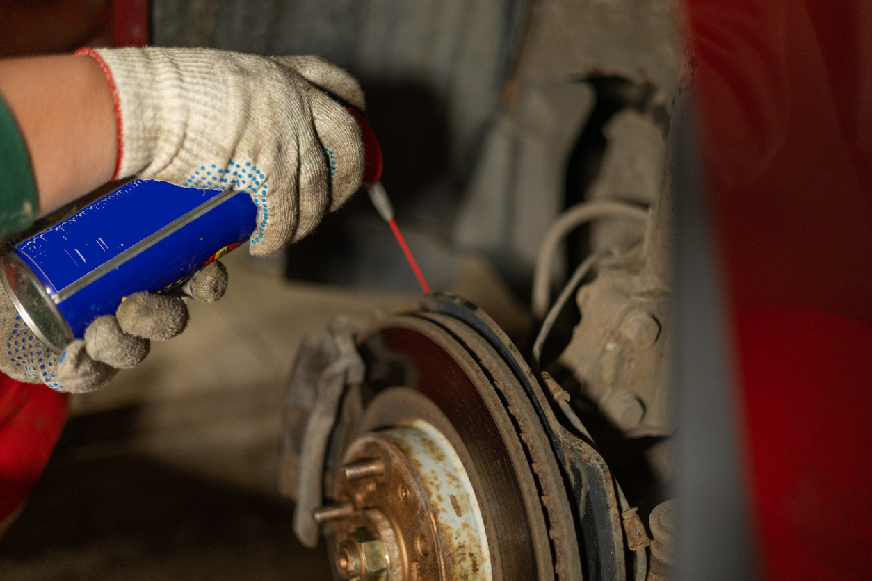 A man is repairing a car in a garage. A man treats rusted bolts with WD-40 solution. Replacing a brake disc on a car in the garage. Concept of a man fixing his car in a garage..